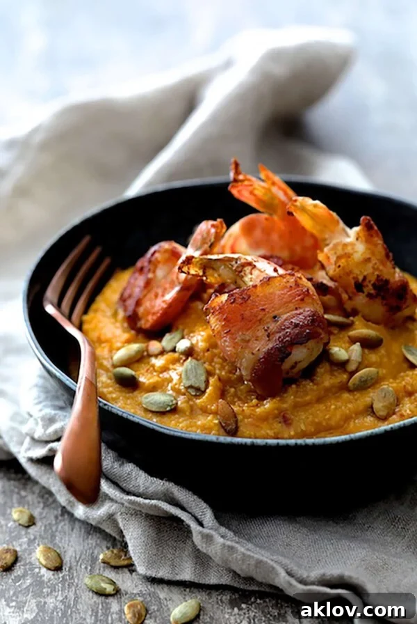 Pumpkin Chipotle and White Cheddar Grits with Bacon Wrapped Shrimp in black bowl garnished with pumpkin seeds.