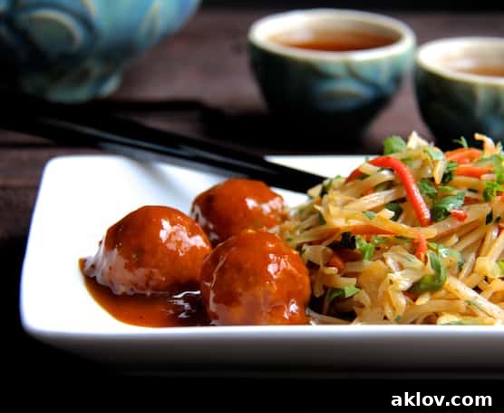 Close-up photo of Hoisin Glazed Pork Meatballs and Rice Noodles with Cabbage and Carrots on a rectangular white plate, with blue teacups in the background.