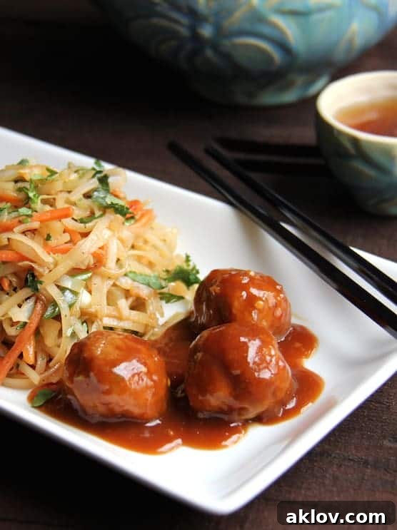 Three Hoisin-Glazed Pork Meatballs on a rectangular white plate with Rice Noodles with Cabbage and Carrots.