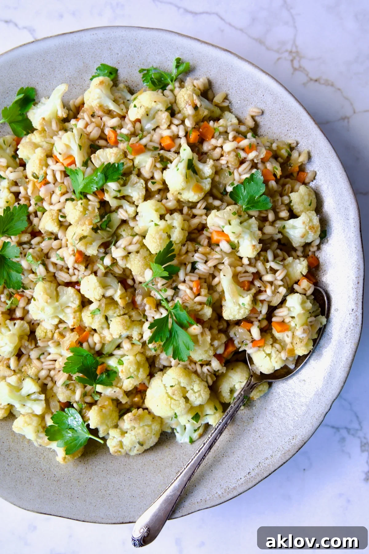 Barley Pilaf with Roasted Cauliflower, garnished with fresh parsley, served in an elegant bowl with a serving spoon.