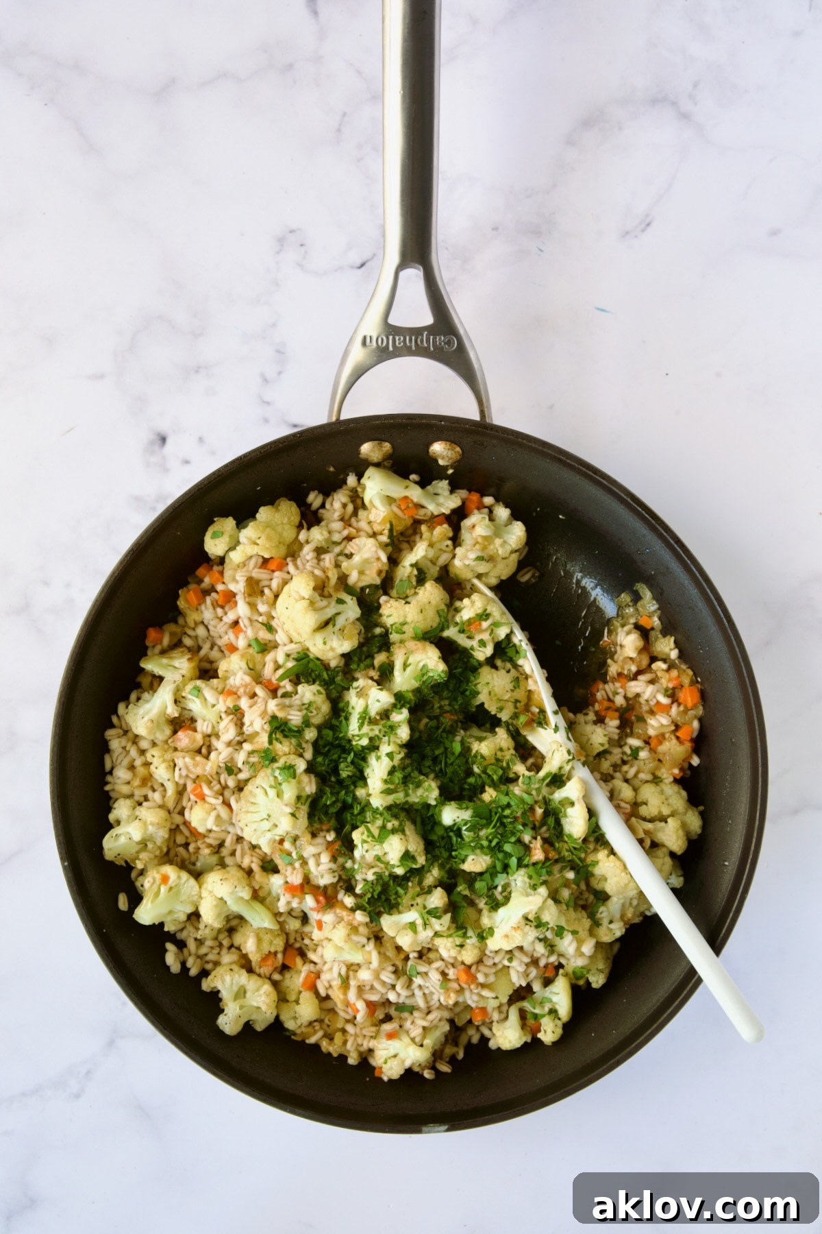 Cauliflower and barley being gently folded into the sautéed aromatics in a nonstick skillet, combining flavors.
