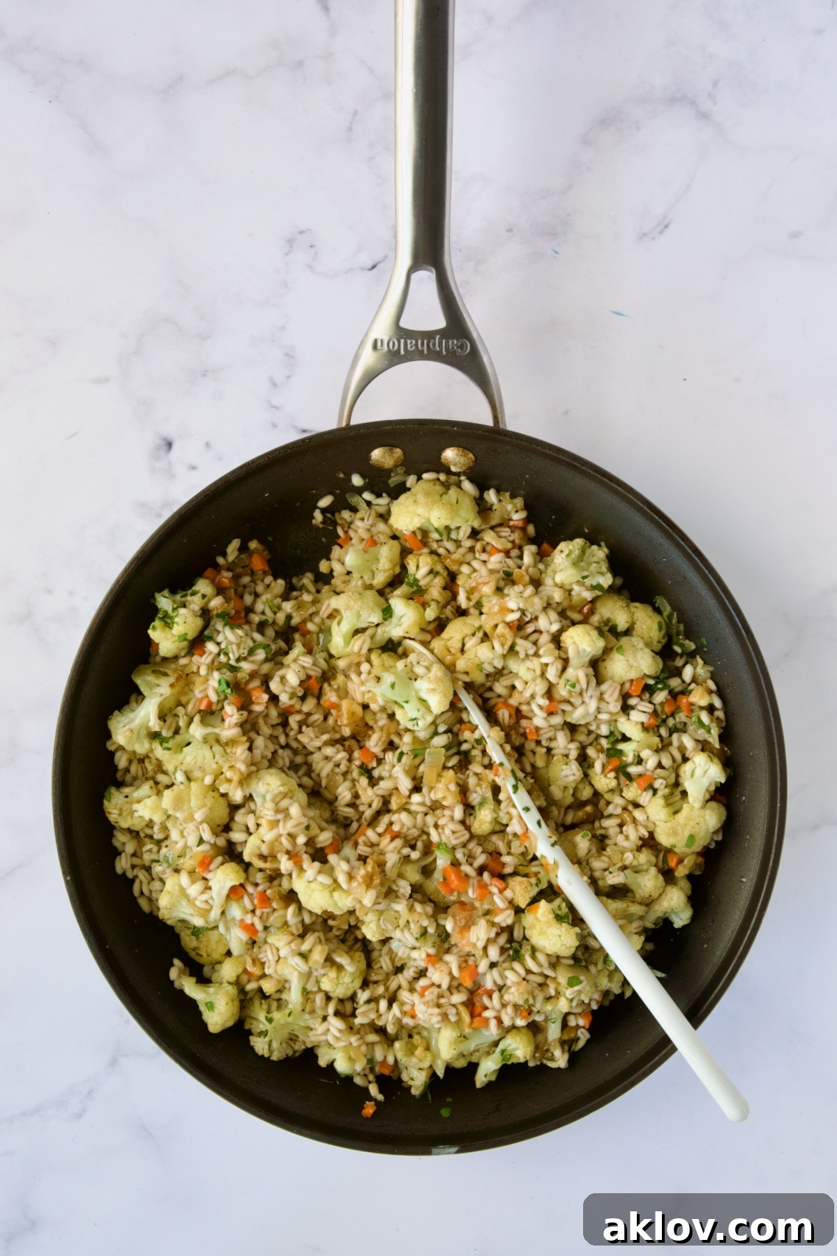 Finished barley pilaf, beautifully combined with cauliflower and aromatics, being stirred in a nonstick skillet.