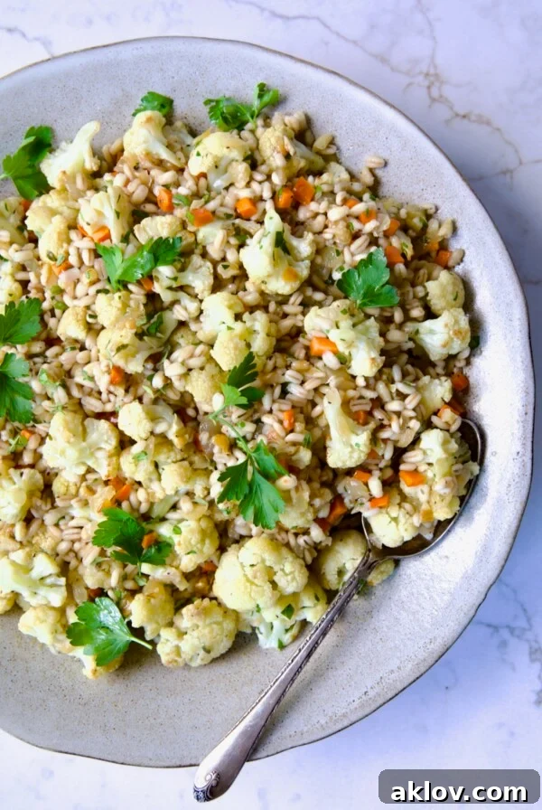 Barley Pilaf with Roasted Cauliflower garnished with fresh parsley in serving bowl with serving spoon.