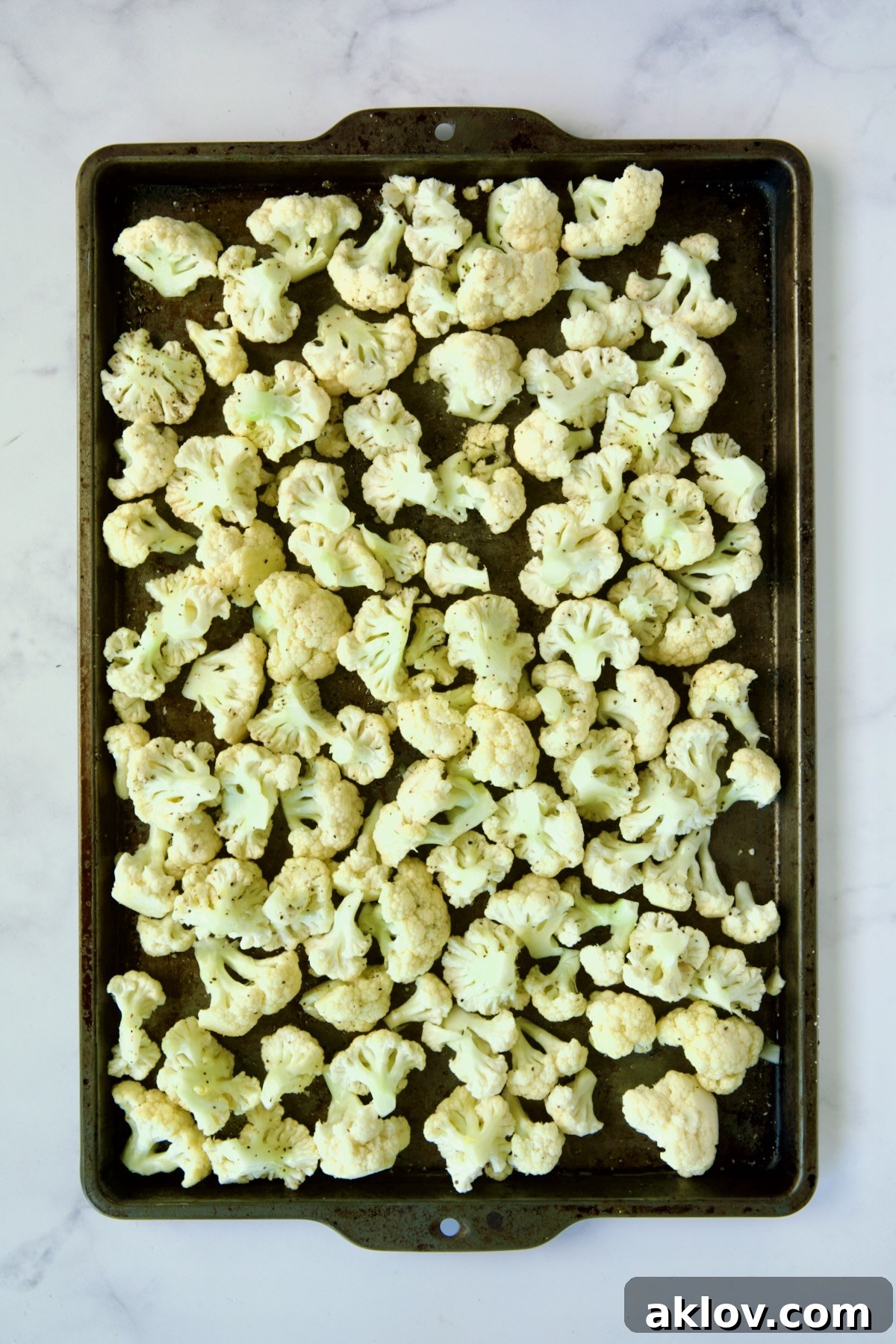 Raw cauliflower florets evenly spread on a rimmed sheet pan, ready for roasting.