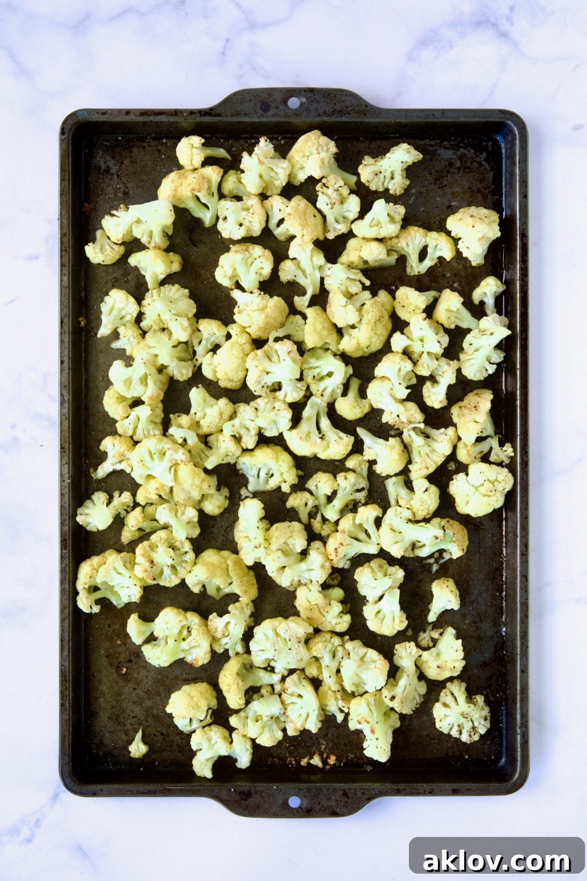 Beautifully roasted cauliflower florets with golden-brown edges on a rimmed sheet pan after cooking.