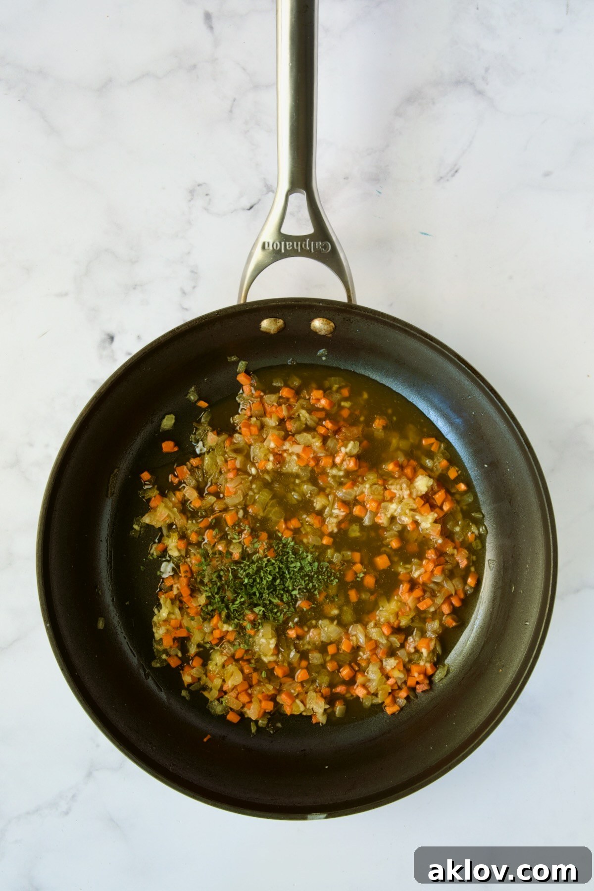 Aromatic mixture of diced onion, carrot, minced garlic, and broth simmering in a nonstick skillet.