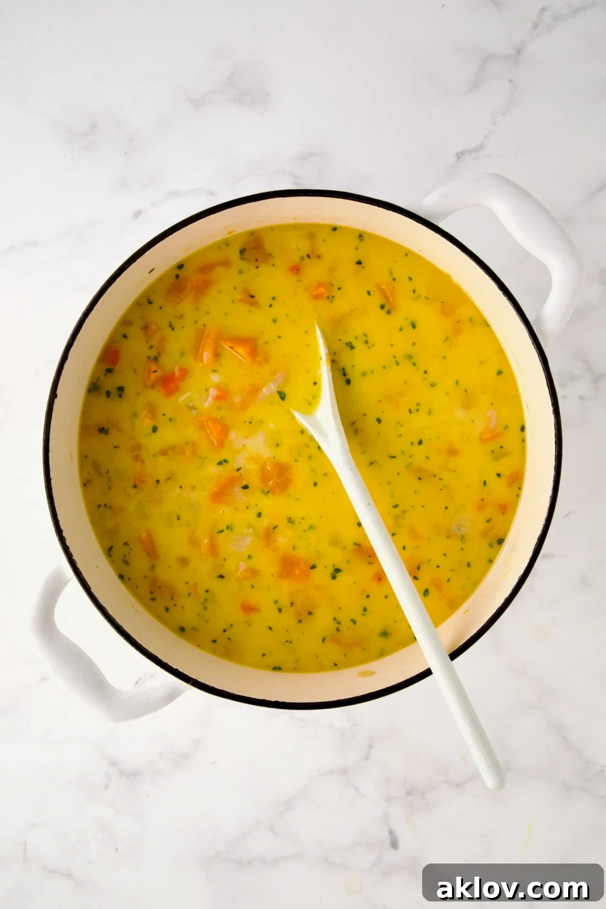 The Butternut Squash Brie Soup mixture being stirred, showing the cheese melting into the rich liquid, creating a creamy texture.
