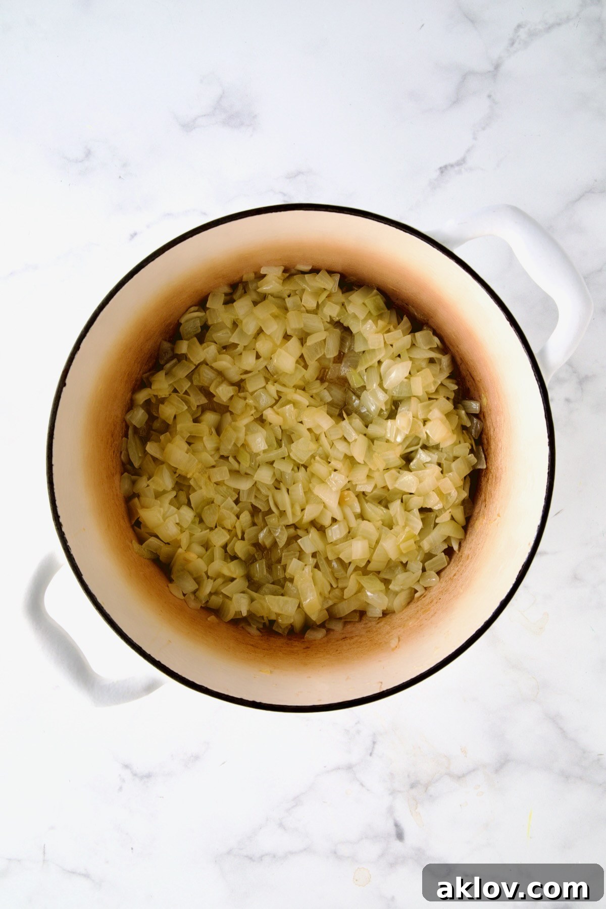 Gently sautéed onions in a white enamel Dutch oven, softened and translucent, forming the aromatic base for the soup.