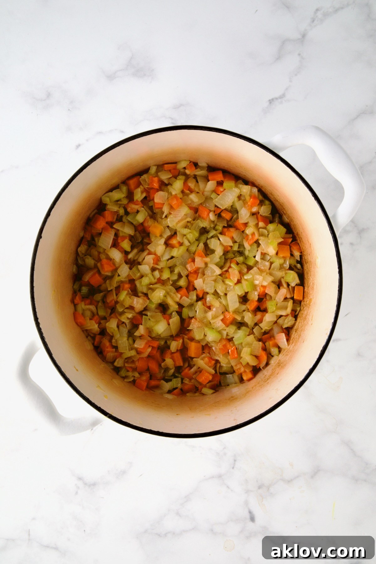 Sautéed onions, celery, and carrots melding together in a white enamel Dutch oven, developing deep flavors.