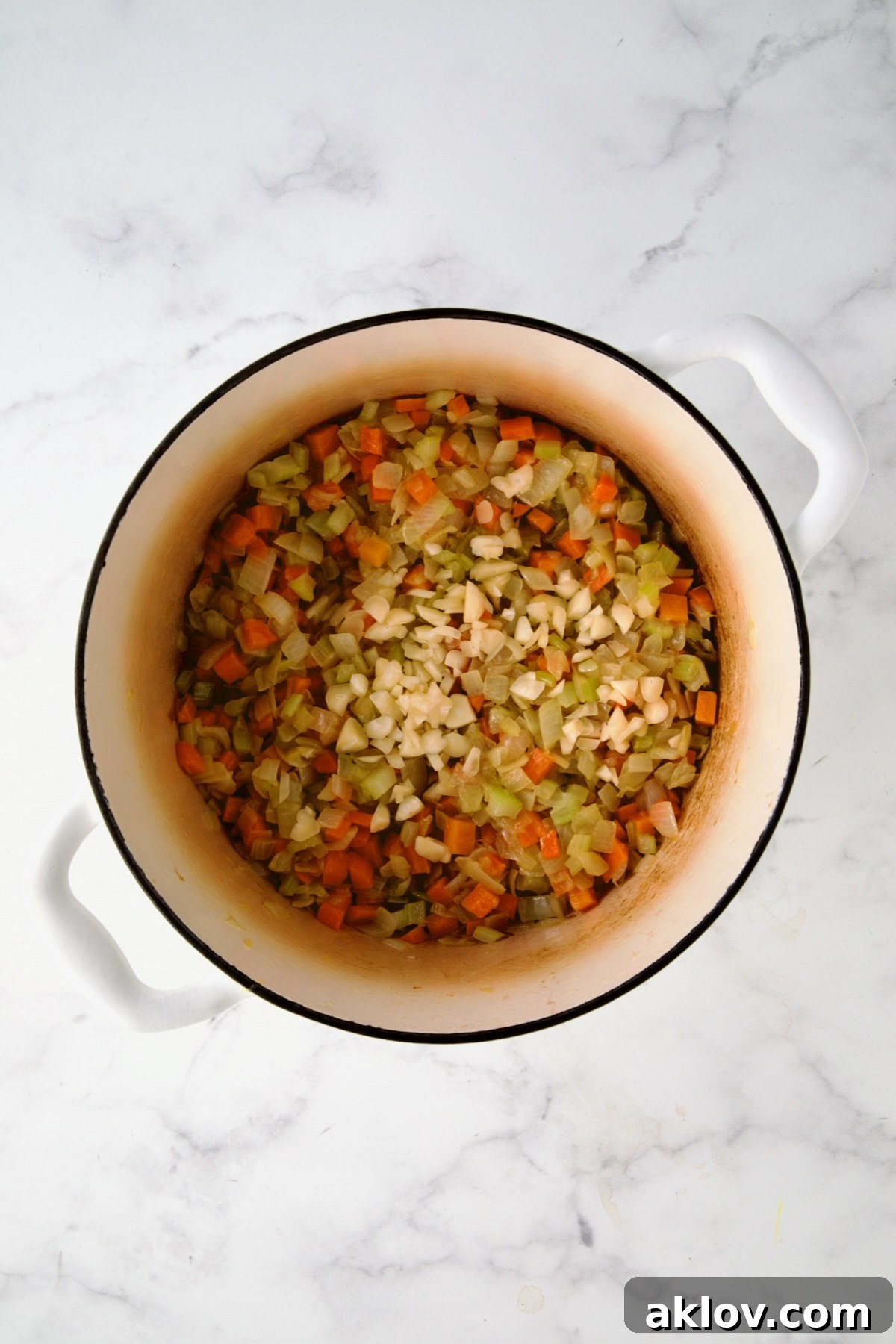 Freshly minced garlic added to the aromatic base of onions, carrots, and celery in the white enamel Dutch oven, ready to release its fragrance.