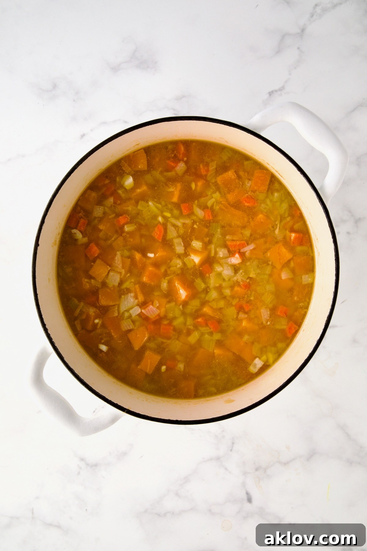 The butternut squash and vegetables gently simmering in broth within the white enamel Dutch oven, allowing flavors to deepen and squash to tenderize.