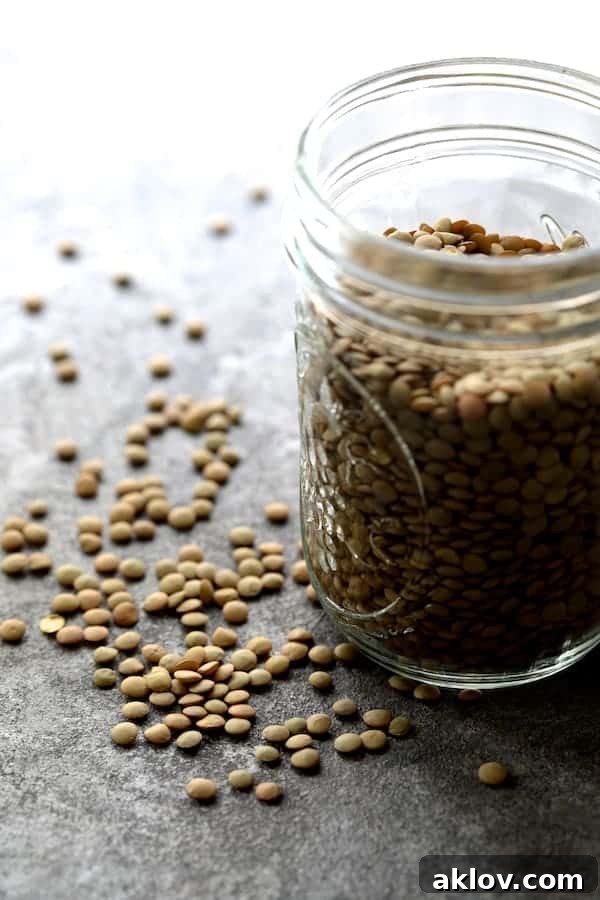 A jar of brown lentils with some scattered on surface.