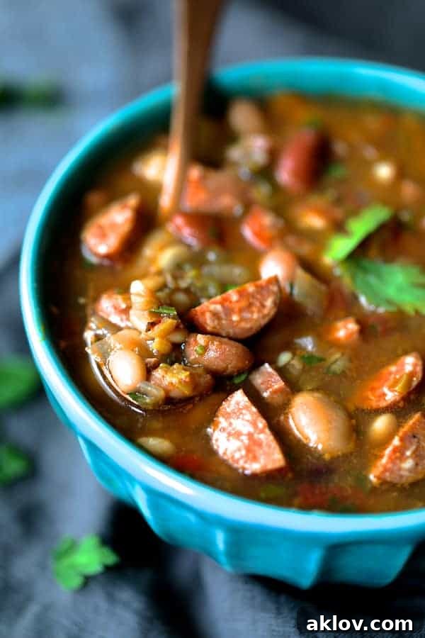 Close-up photo of Slow Cooker Cajun 15 Bean Soup with Andouille Ham and Bacon in aqua-colored bowl with copper spoon.