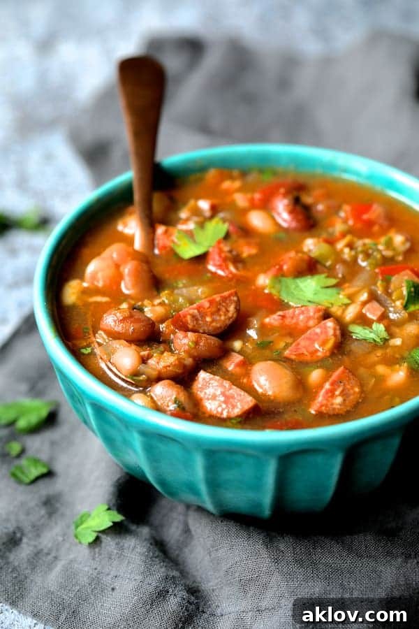 Photo of Slow Cooker Cajun 15 Bean Soup with Andouille Ham and Bacon in aqua-colored bowl with copper spoon on gray napkin garnished with parsley leaves.