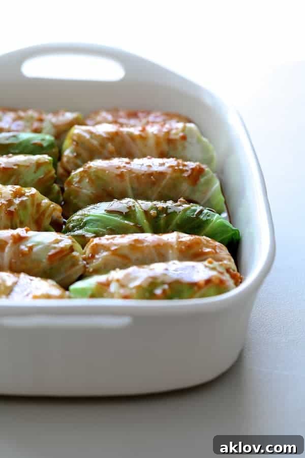 Asian Spiced Pork Cabbage Bundles 6 Photo of uncooked cabbage rolls in a white baking pan with the savory Asian sauce drizzled generously over the top, ready for baking.