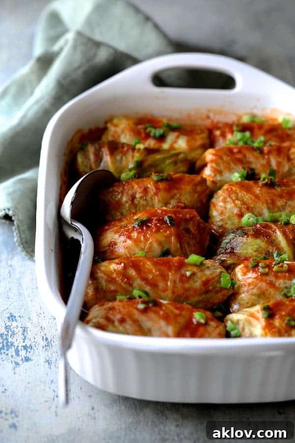 Asian Spiced Pork Cabbage Bundles 7 Photo of perfectly cooked Spicy Asian Pork Cabbage Rolls in a white baking dish on a blue background, accompanied by a green dish towel and a white metal spoon.
