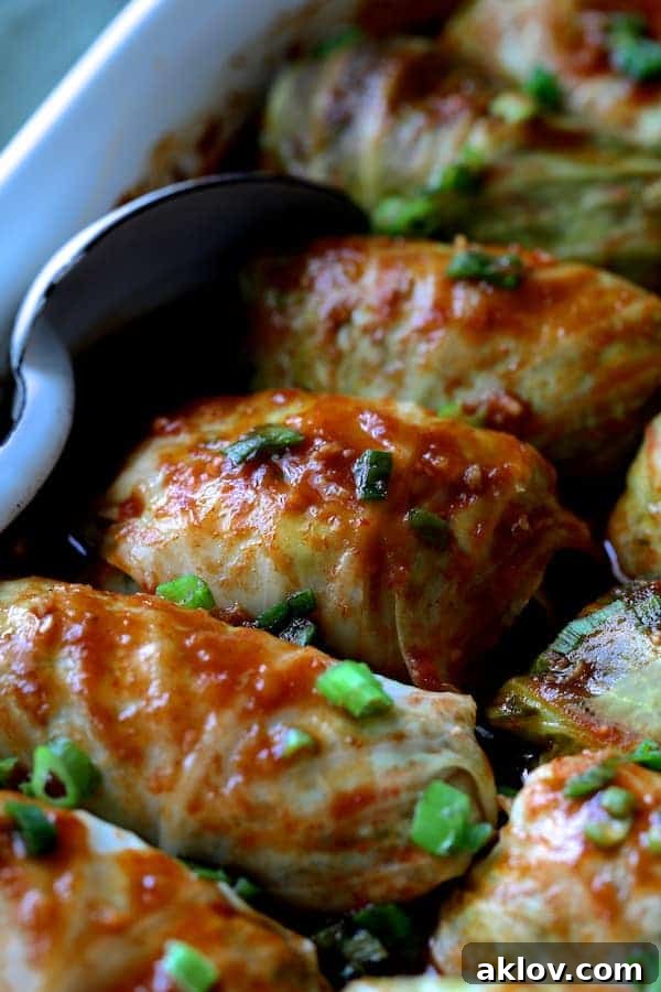 Asian Spiced Pork Cabbage Bundles 9 Another close-up photo of cooked Spicy Asian Pork Cabbage Rolls in a white baking dish with a white metal spoon, highlighting the rich sauce and tender cabbage.