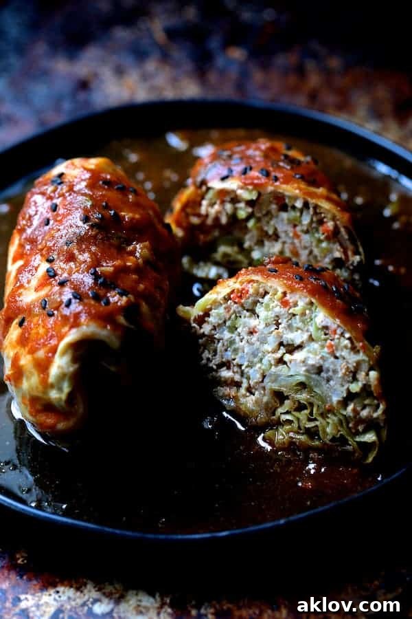 Asian Spiced Pork Cabbage Bundles 10 Photo showcasing Spicy Asian Pork Cabbage Rolls cut in half on a black plate, garnished with black sesame seeds, revealing the flavorful filling.