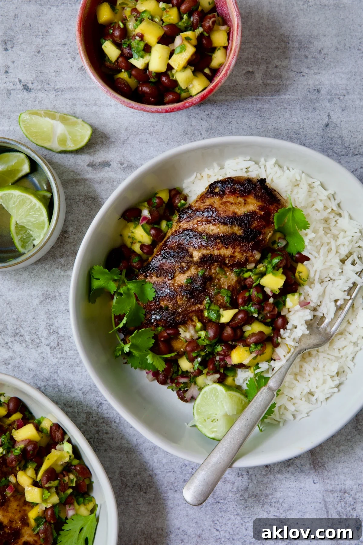 Caribbean Jerk Chicken with Mango Black Bean Salsa in white bowl garnished with cilantro and squeezed lime wedges.