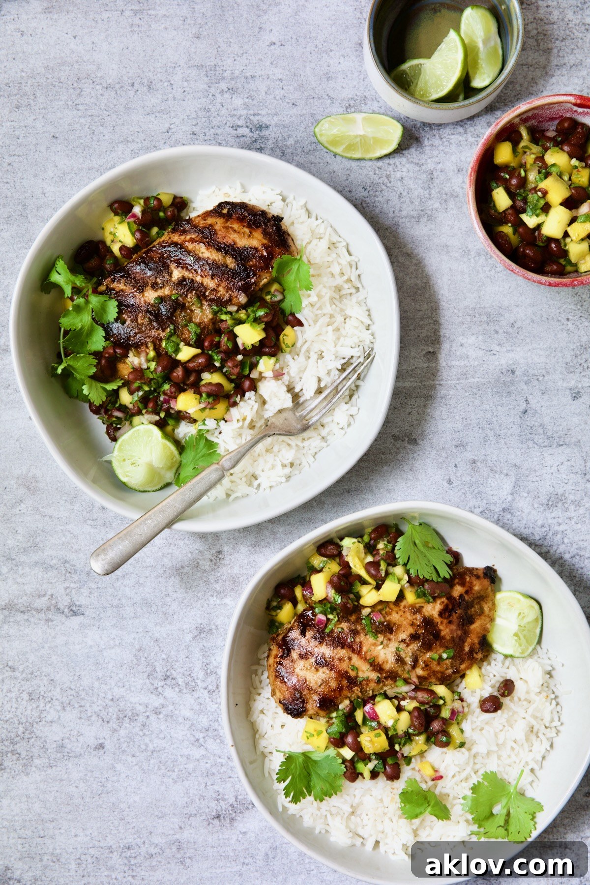 Two servings of Caribbean Jerk Chicken with Mango Black Bean Salsa with rice in white bowls.