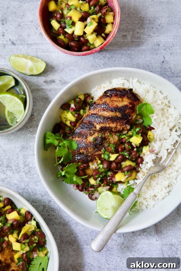Caribbean Jerk Chicken with Mango Black Bean Salsa in white bowl garnished with cilantro and squeezed lime wedges.