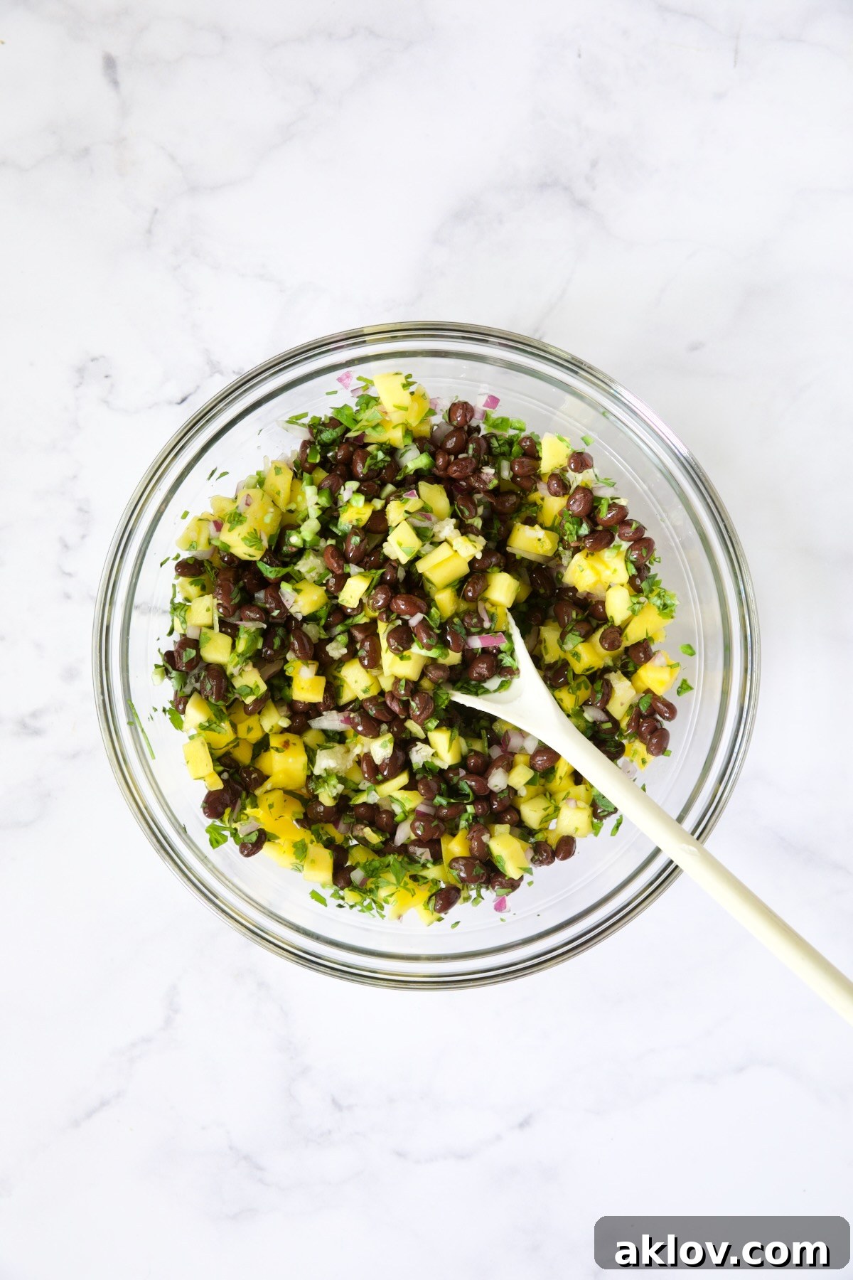 Black Bean Mango Salsa in glass bowl being stirred with white spoon.