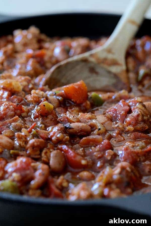 Photo of Skillet Turkey Pinto Bean Chili being stirred in cast iron skillet with a wooden spoon. The rich red chili is visible.