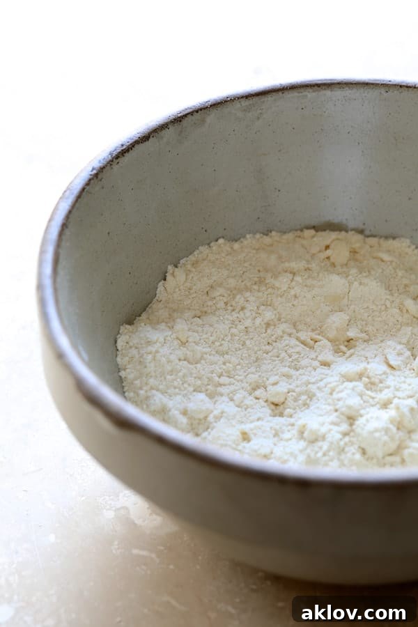 Photo of biscuit mixture in a stoneware bowl before forming and baking. The dry ingredients and shredded cheese are visible.