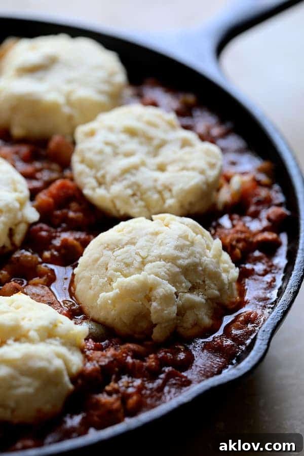Close-up photo of uncooked biscuits arranged on the chili in cast iron skillet before being baked. The rich chili peeks out from between the biscuit dough.