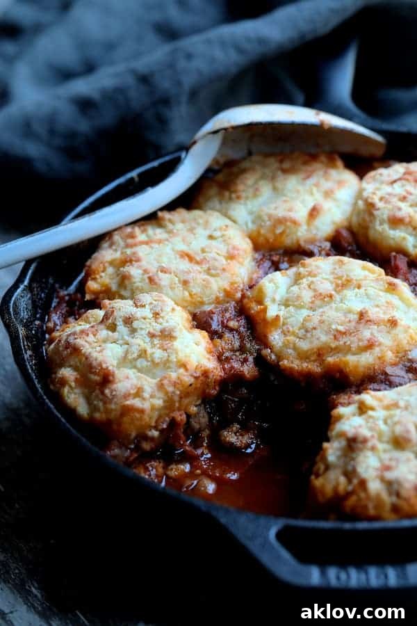Photo of Skillet Turkey Pinto Bean Chili with Pepper Jack Biscuit Topping with a biscuit and some of the chili served to show interior of chili. A spoonful of chili and a biscuit are in a bowl, showcasing the textures.
