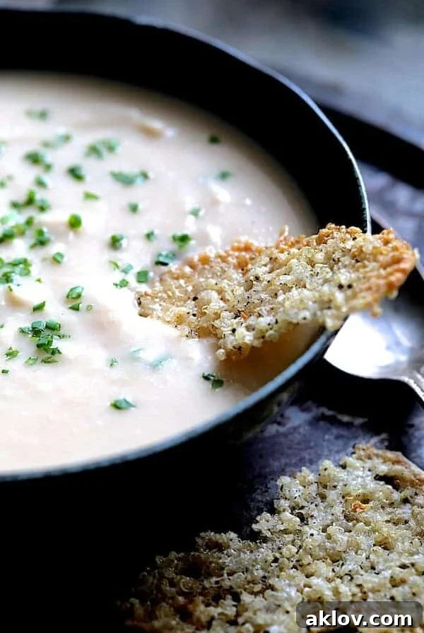 Creamy White Bean, Rutabaga and Roasted Garlic Soup with Quinoa Parmesan Crisps - Close-up shot of soup in black bowl garnished with fresh chives