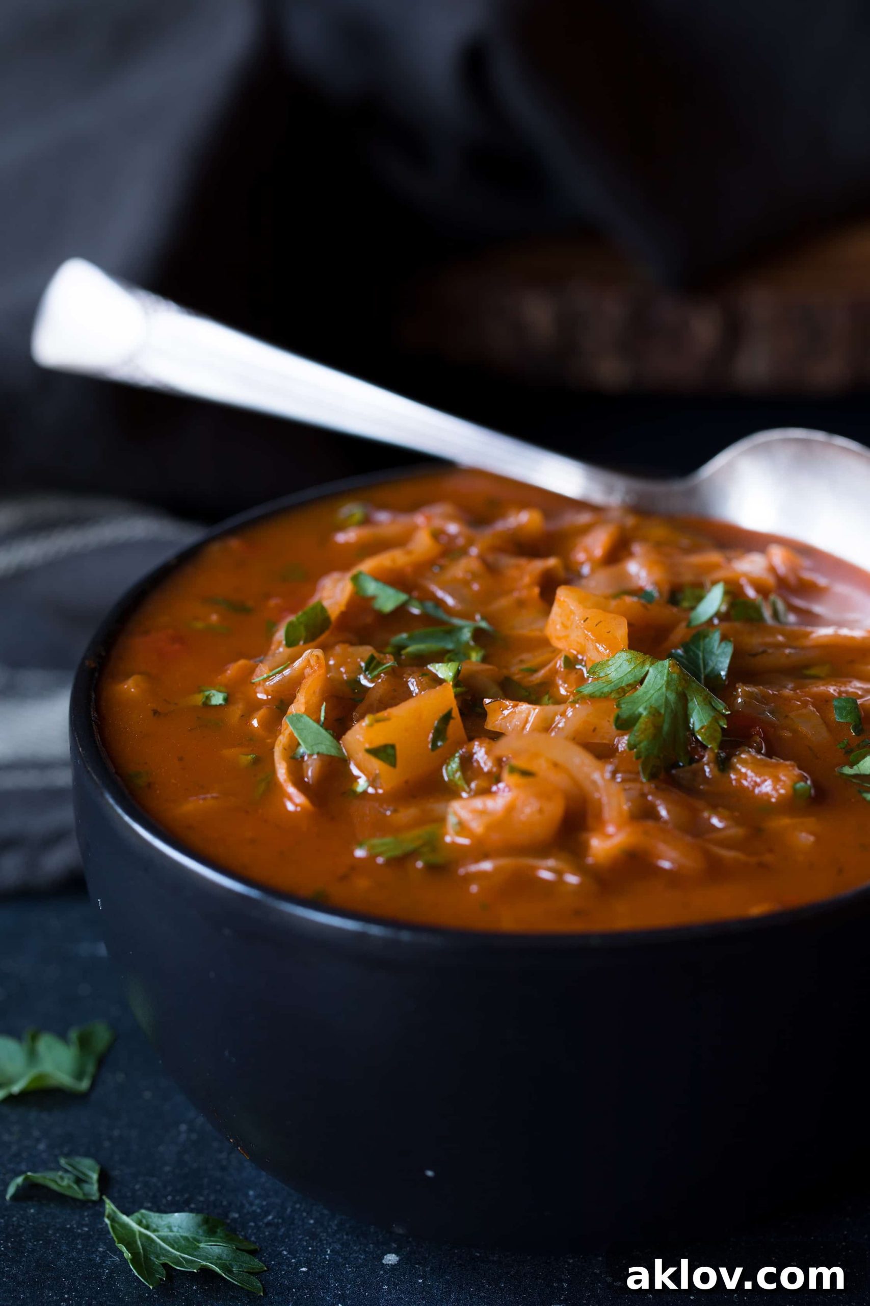 Close-up photo of Rustic Cabbage and Root Vegetable Soup in a black bowl with a spoon, highlighting the rich texture and vibrant vegetables.