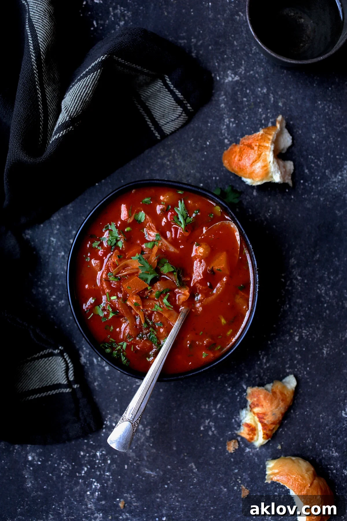Rustic Cabbage and Root Vegetable Soup in a black bowl garnished with parsley, served with pieces of crusty bread scattered around.