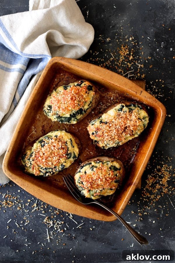 Photo of Spinach Parmesan Ranch Twice Baked Potatoes nestled in a clay baking dish, accompanied by a blue striped towel for presentation.