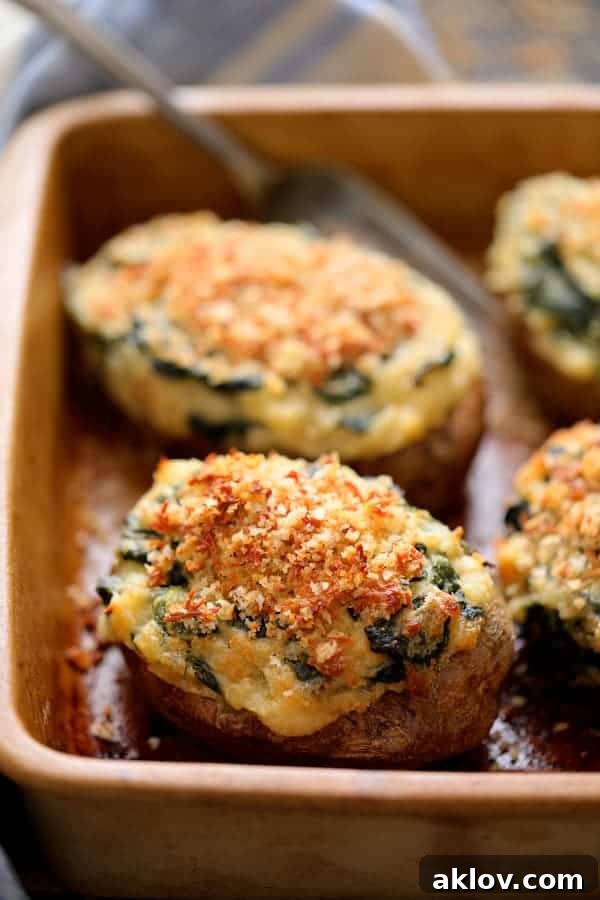 Close-up photo highlighting the texture and topping of Spinach Parmesan Ranch Twice Baked Potatoes in a clay baking dish, with a serving fork.