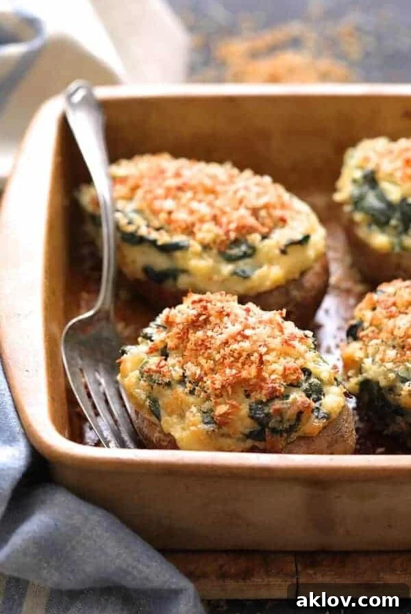 Spinach Parmesan Ranch Twice Baked Potatoes close up shot in clay baking dish with serving fork and blue striped towel.