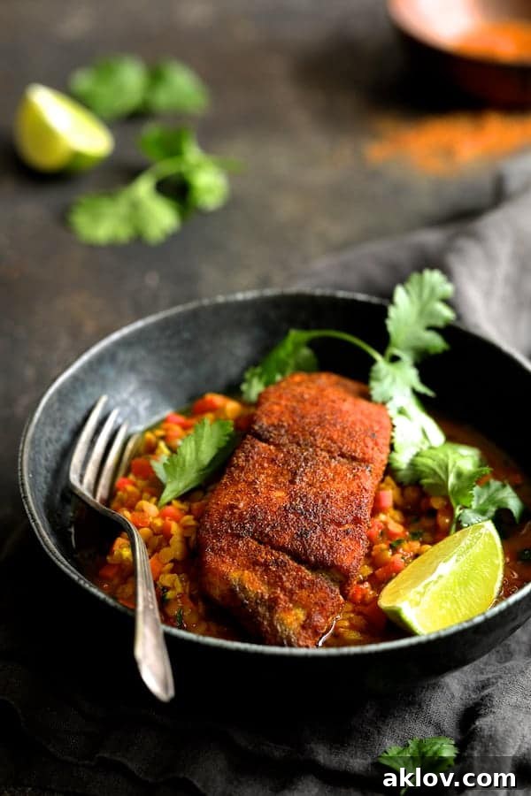 Masala-Crusted Sea Bass with Hearty Red Lentil Daal 6 A single serving of Indian Spiced Sea Bass with Braised Red Lentils, garnished with vibrant cilantro sprigs and a fresh lime wedge, presented in an elegant bowl with a fork.