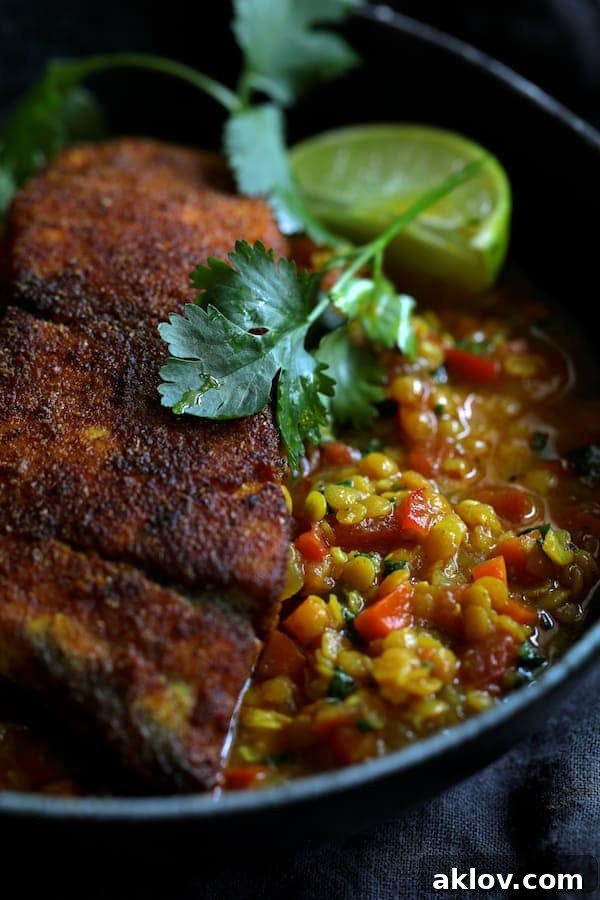 Masala-Crusted Sea Bass with Hearty Red Lentil Daal 7 A close-up view of a single serving of Indian Spiced Sea Bass with Braised Red Lentils, highlighting the tender fish, creamy lentils, fresh cilantro, and a bright lime wedge.