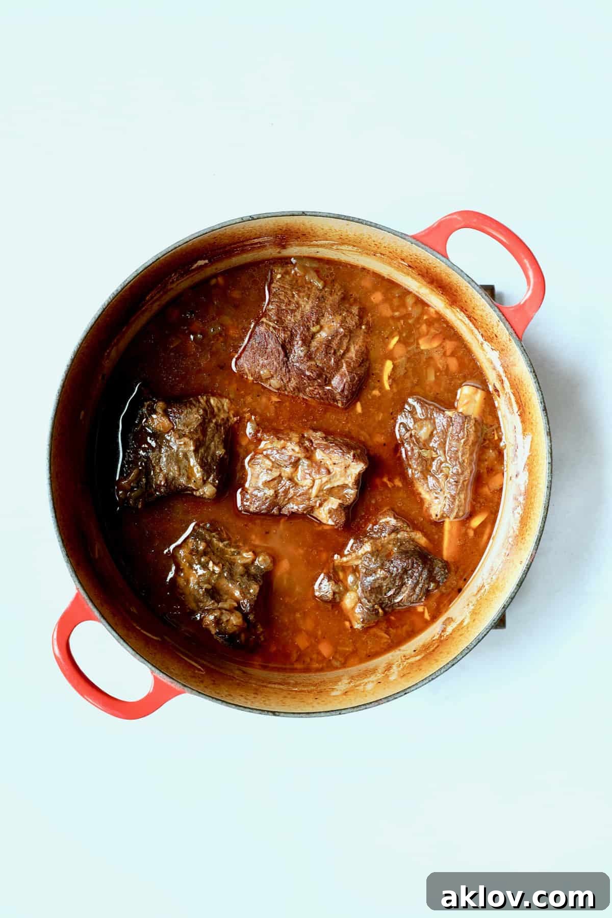 Rich Stout Braised Beef Short Ribs, tender and glistening, in a red Dutch oven after the braising process, with the flavorful sauce ready for skimming.