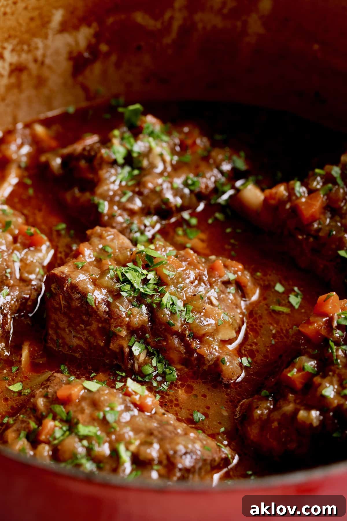 A close-up of a deep red Dutch oven filled with glistening, tender Stout Braised Beef Short Ribs, submerged in their rich, dark sauce, promising profound flavor.