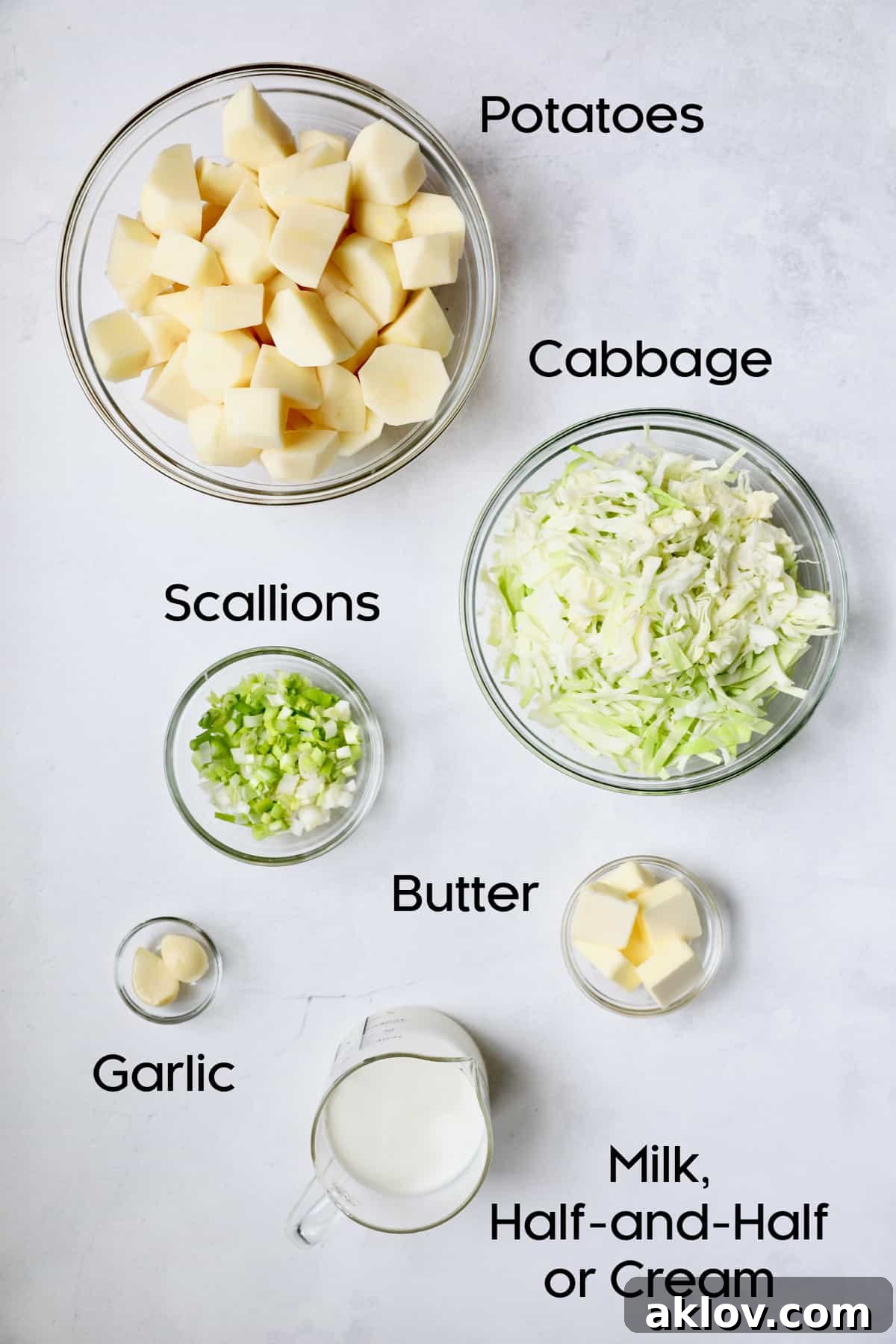 A pristine display of fresh ingredients for Colcannon in clear glass bowls, featuring perfectly cubed Russet potatoes, finely sliced green cabbage, bright scallions, and minced garlic, all ready for preparation.