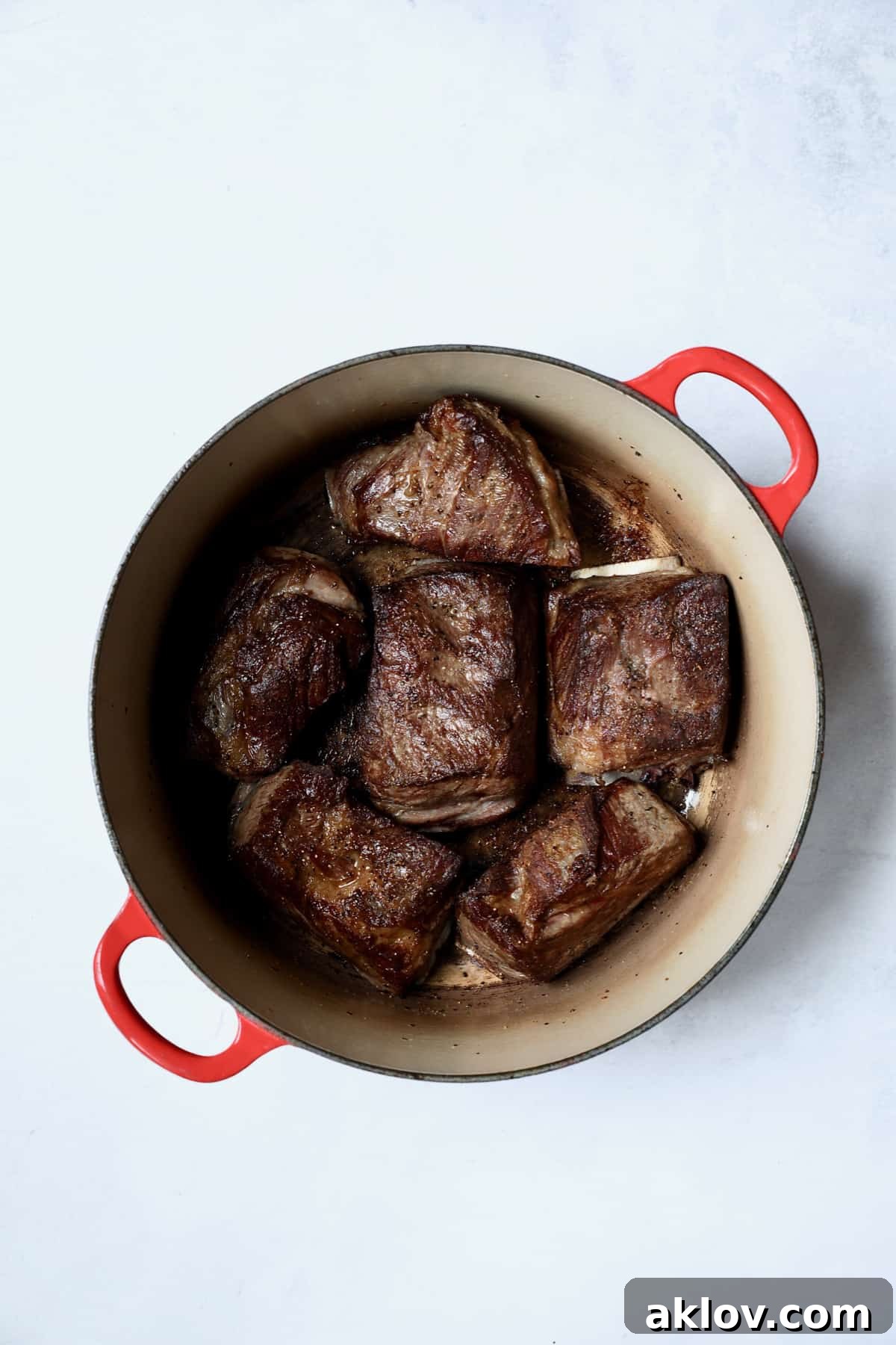 Perfectly browned beef short ribs sizzle in a vibrant red Dutch oven, showcasing a rich, caramelized crust achieved through initial searing, ready for the next stage of braising.