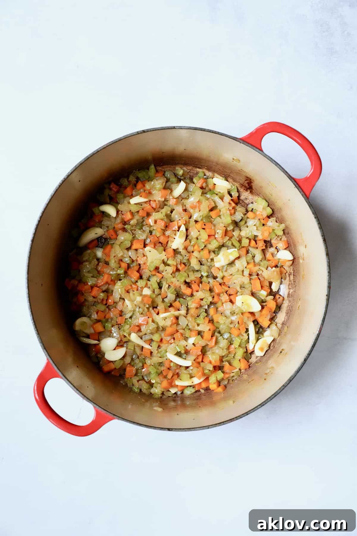 Aromatic diced onions, celery, and carrots, now beautifully softened and mingled with freshly sliced garlic, gently cook in a red Dutch oven, building the flavorful foundation for the short ribs.