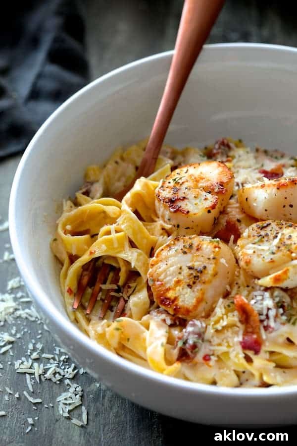 Close-up of perfectly Seared Sea Scallops with Spicy Bacon and Sun Dried Tomato Alfredo Sauce, served over tagliatelle pasta and twirled around a copper fork.