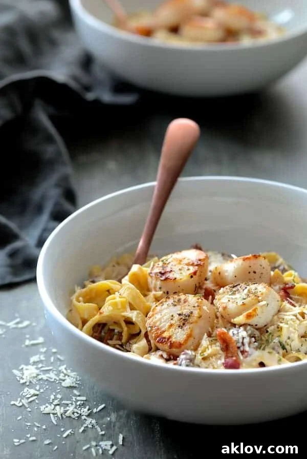 Seared Sea Scallops with Spicy Bacon Sun Dried Tomato Alfredo Sauce in white bowl with pasta twirled around a copper fork, garnished with fresh herbs.