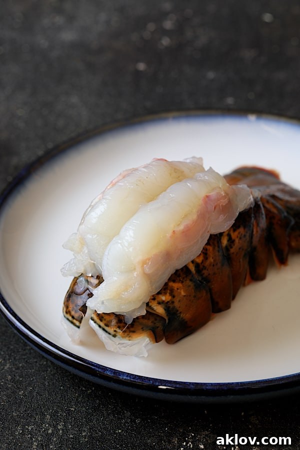 Photo of uncooked lobster tail with meat on top of the shell on white plate.