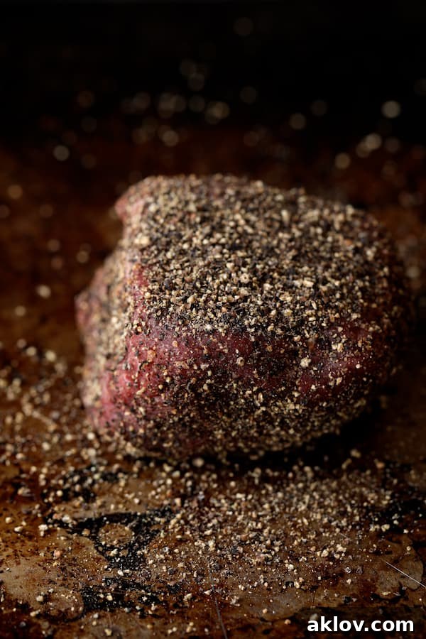 Photo of uncooked steak encrusted with black peppercorns.