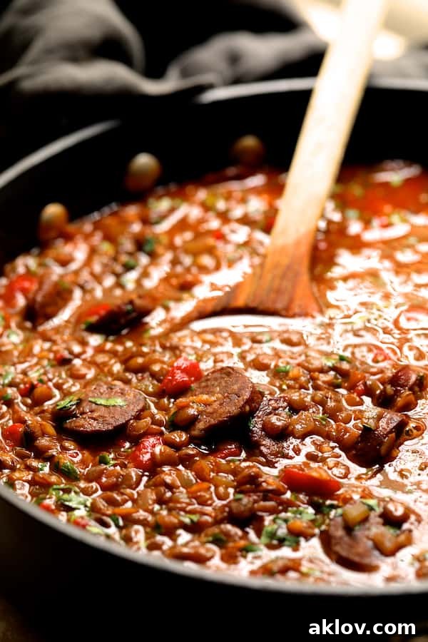 Close-up photo of Soupy Spanish Lentils with Chorizo cooking in a deep pot, being stirred with a wooden spoon.