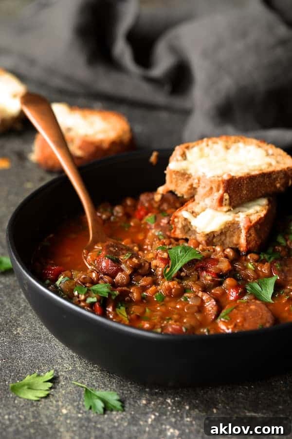 A single serving of Soupy Spanish Lentils with Chorizo and Manchego Toast in a black bowl, garnished with vibrant fresh parsley, ready to be enjoyed.