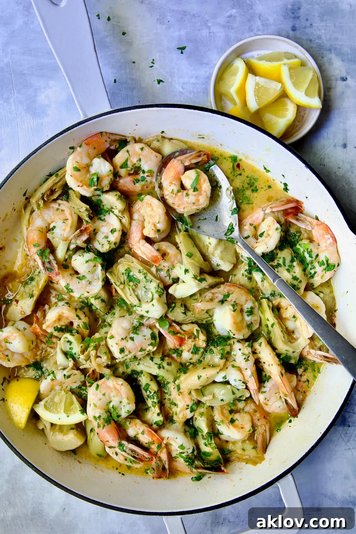 Shrimp Scampi with Artichokes in white enamel cast iron pan with serving spoon.